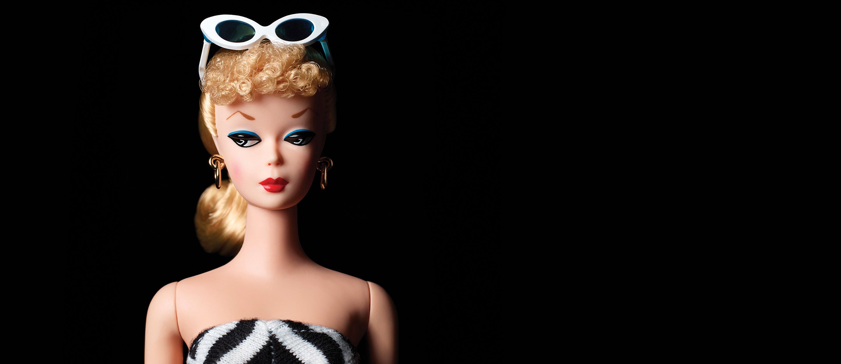 Vintage-style Barbie doll with cat-eye sunglasses, bold blue eye  makeup, and a black-and-white striped top